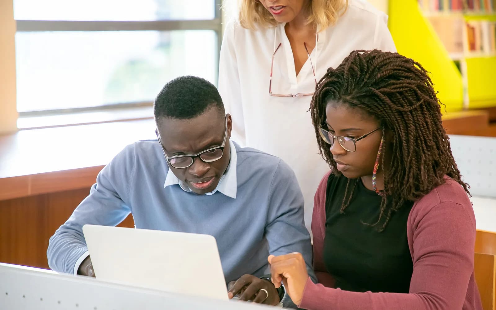 Two adult learners reviewing work together on a laptop with guidance from a tutor