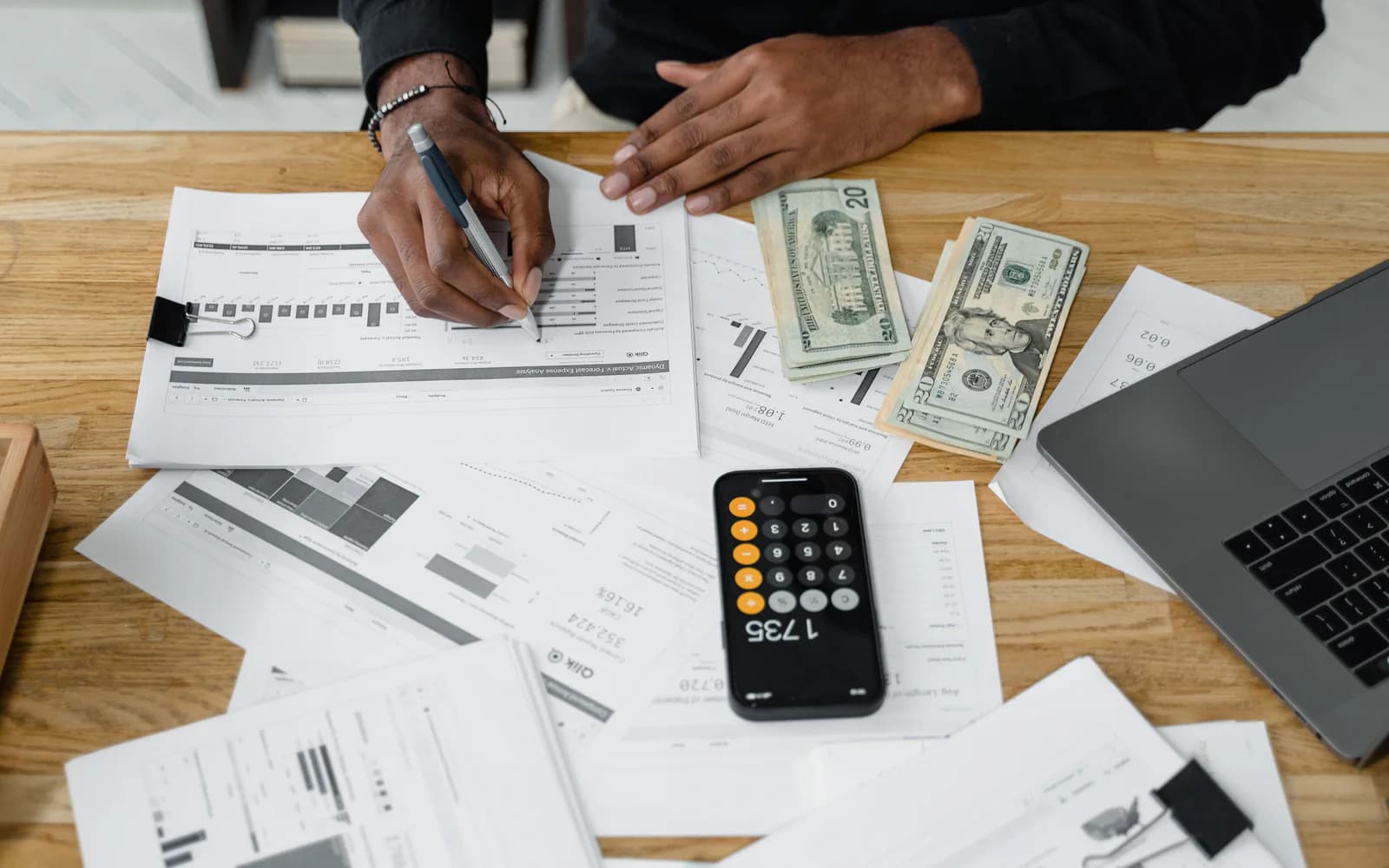 Accountant reviewing financial reports with a calculator and laptop on a wooden desk